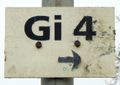 Een oud, verweerd bord met de inscriptie 'Gi 4' en een pijl die naar rechts wijst.