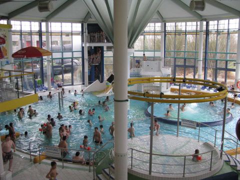 Une piscine intérieure pleine de gens avec des toboggans et des aires de jeux. De grandes fenêtres laissent entrer beaucoup de lumière du jour.