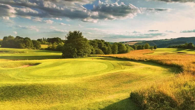 Eine schöne Golfplatzlandschaft mit grünem Rasen und sanften Hügeln. Der Himmel ist teilweise bewölkt und die Umgebung ist friedlich.