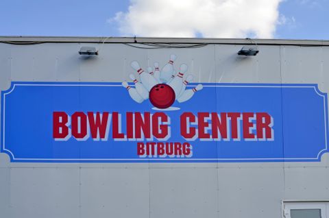 Ein Schild mit der Aufschrift "BOWLING CENTER BITBURG" in leuchtenden Farben. Es zeigt eine Bowlingkugel und Pins, die das Bowlen darstellen.