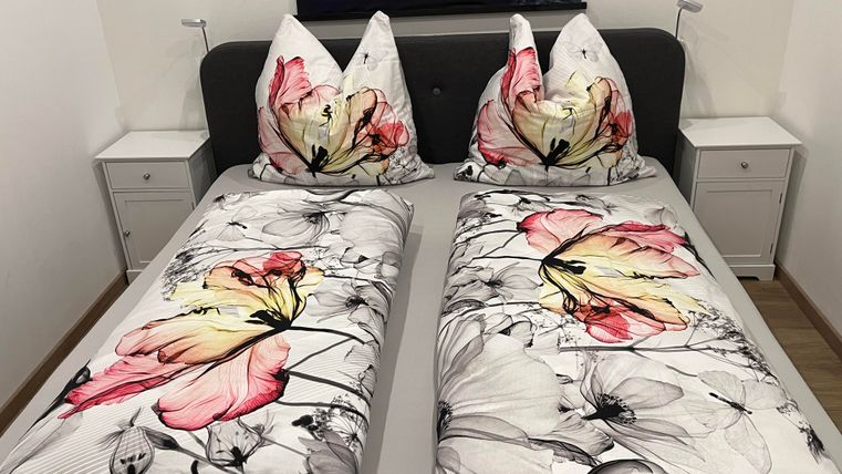 Een gezellige slaapkamer met een tweepersoonsbed en kleurrijke dekbedden met bloemenpatroon. Naast het bed staan twee nachtkastjes.