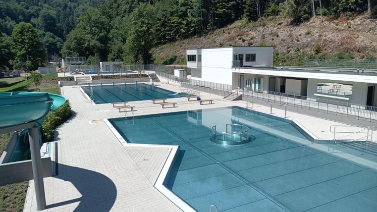 Een modern zwembad met meerdere bassins en helder blauw water. De inrichting is omringd door bomen en heeft veel ruimte om te ontspannen.