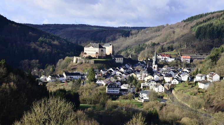 Blick auf Schloss Malberg und das umliegende Dorf in einer hügeligen Landschaft.