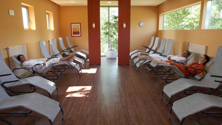 Een ontspannende rustruimte met ligstoelen en zachte verlichting. Enkele personen ontspannen in comfortabele badjassen.