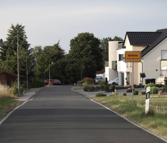 Ortseingang von Idenheim mit Straßenschild, modernen Wohnhäusern und gepflegten Vorgärten entlang einer ruhigen Straße., © Thomas Neises