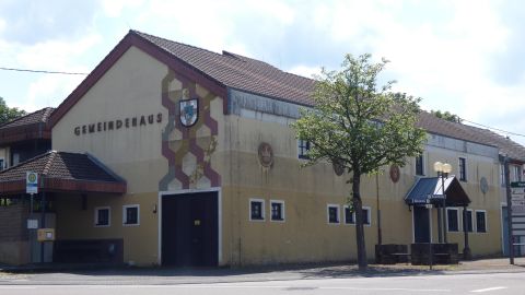 Een gemeentelijk gebouw met het opschrift "Gemeentehuis". Het is omgeven door bomen en heeft een functionele bouwstijl.