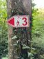 Wegmarkierung mit der Nummer 3 an einem Baum im Wald.