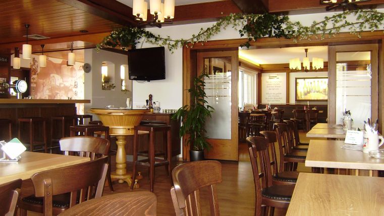 Ein gemütliches Restaurant mit Holztischen und Stühlen. Die lichten Wände und Deckenlichter schaffen eine einladende Atmosphäre.