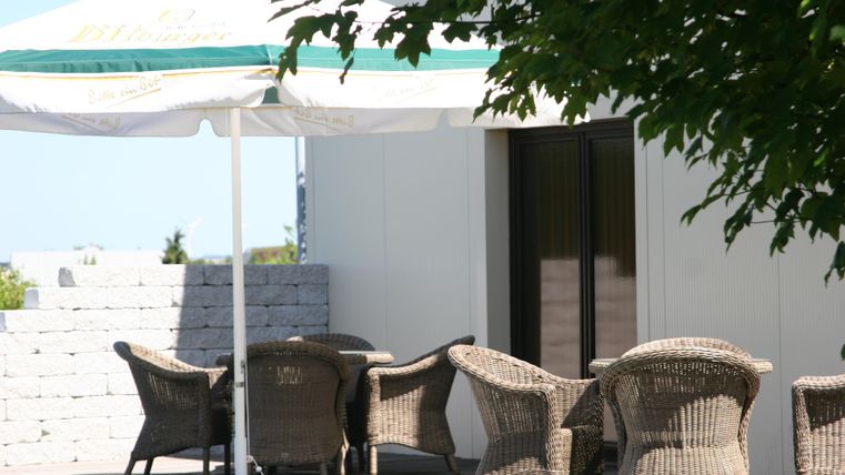 Ein gemütlicher Außenbereich mit einer Markise und einem Tisch. Rund um den Tisch stehen mehrere geflochtene Stühle.