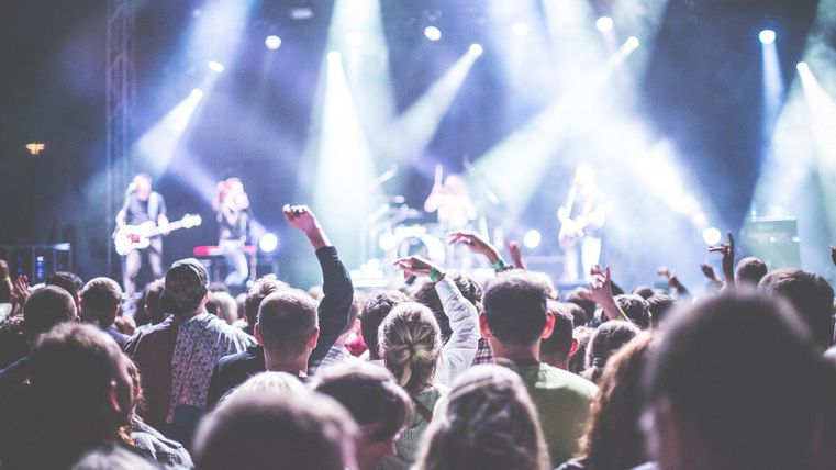 Ein Konzert mit vielen begeisterten Zuschauern vor der Bühne. Die Künstler spielen unter bunten Lichtern und strahlen Energie aus.
