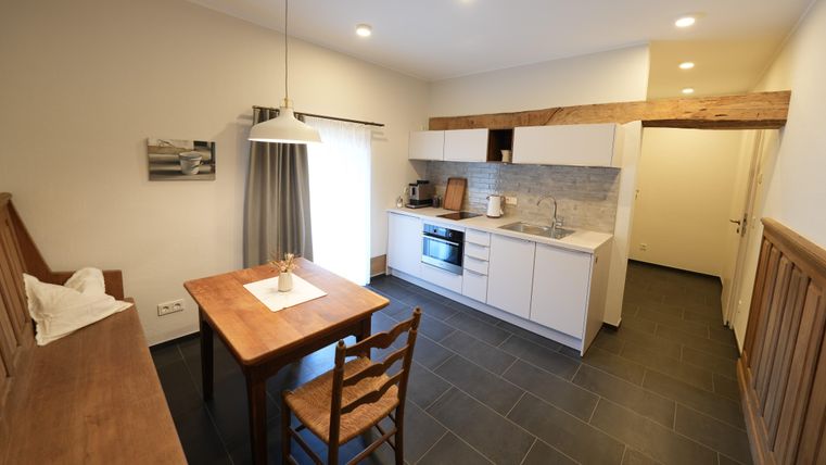 Een moderne keuken met een eettafel van hout en stoelen. De ruimte is licht en vriendelijk, met grote ramen en een modern layout.