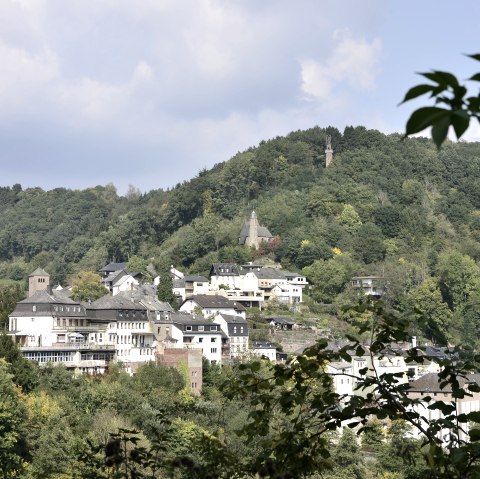 Panoramisch uitzicht op Kyllburg met huizen en een kerk op een beboste heuvel onder een blauwe lucht., © TI Bitburger Land