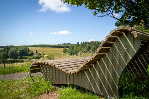 Holzliegebank mit Blick auf eine grüne Landschaft und blauen Himmel in Neidenbach.