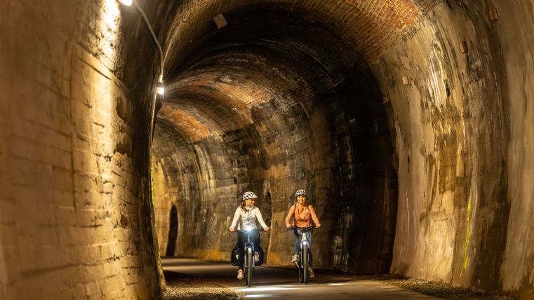 Zwei Radfahrer fahren durch einen beleuchteten Tunnel auf einer ehemaligen Bahntrasse.