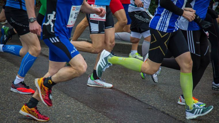 Eine Gruppe von Läufern beim Wettlauf. Die Teilnehmer tragen sportliche Kleidung und verschiedene Laufschuhe.