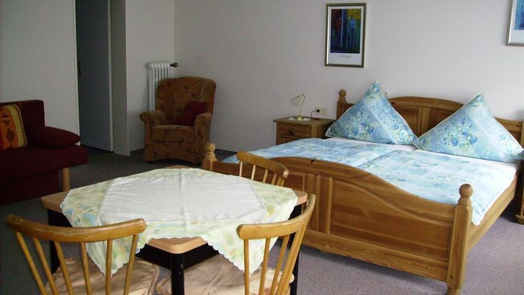 Een gezellige kamer met een tweepersoonsbed en een rode bank. De ruimte bevat een tafel met stoelen en een aangename sfeer.