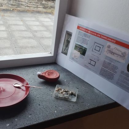 Ein roter Teller und eine kleine Schale liegen auf einer Fensterbank. Daneben steht ein Informationsblatt mit textlichen Erklärungen.