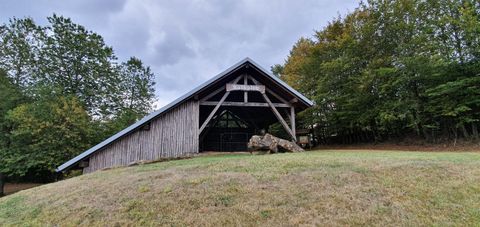 Een groot, modern houten gebouw staat op een groene weide. Op de achtergrond zijn bomen en een bewolkte lucht te zien.