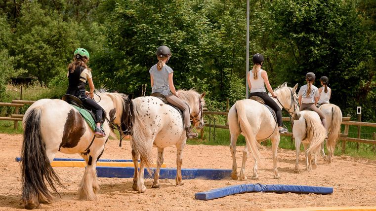 Reiterinnen auf Pferden im Sandbereich für das Training. Sie üben auf verschiedenen Hindernissen unter einem klaren Himmel.