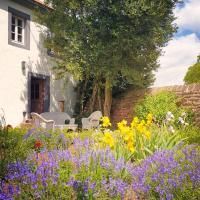 Un beau jardin devant une maison avec des fleurs colorées et un coin salon confortable. À l'arrière-plan, on peut voir des arbres et un ciel dégagé.