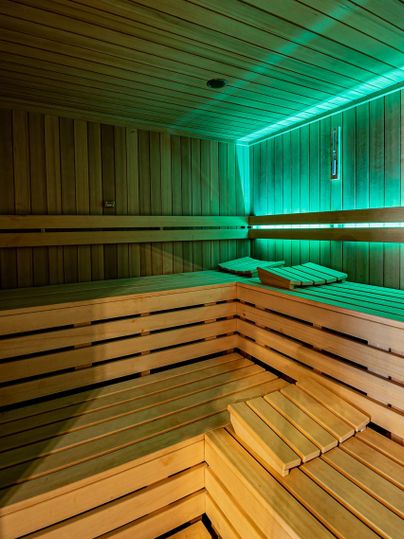 A modern sauna with wooden benches and soft lighting. The walls are made of light wood, creating a relaxing atmosphere.