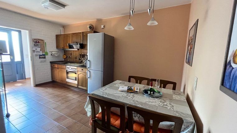 Eine helle Küche mit Holzschränken und einem modernen Kühlschrank. Ein Tisch mit Stühlen steht in der Mitte des Raumes.