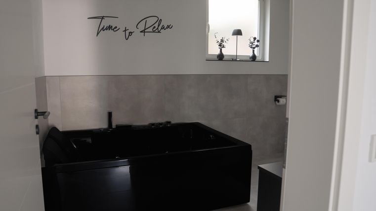 Ein modernes Badezimmer mit einer schwarzen Badewanne. An der Wand steht der Schriftzug „Time to Relax“.
