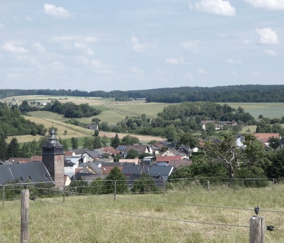Panoramic view of Gransdorf with a church in the foreground, surrounded by houses and green countryside under a blue sky., © TI Bitburger Land