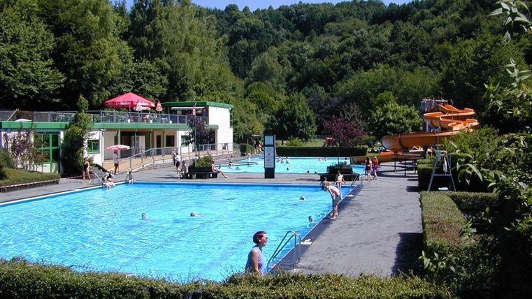 A beautiful swimming area with two pools and a slide. The surroundings are green and inviting.