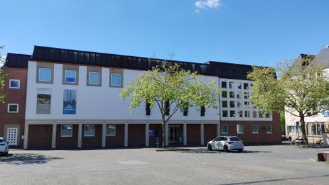 Ein modernes Gebäude mit mehreren Fenstern und Bäumen im Vordergrund. Der Himmel ist klar und blau.