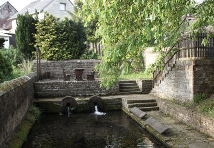 Alter Waschplatz mit Wasserbecken, Steinmauern und Treppen, umgeben von grüner Vegetation und Bäumen., © Monika Bach