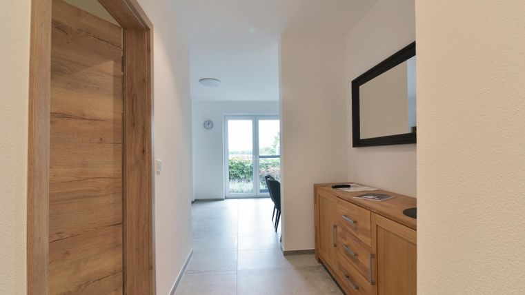 Ein heller Flur mit Holzdetails und einer modernen Spiegelwand. Im Hintergrund sind Fenster, die viel Licht hereinlassen.