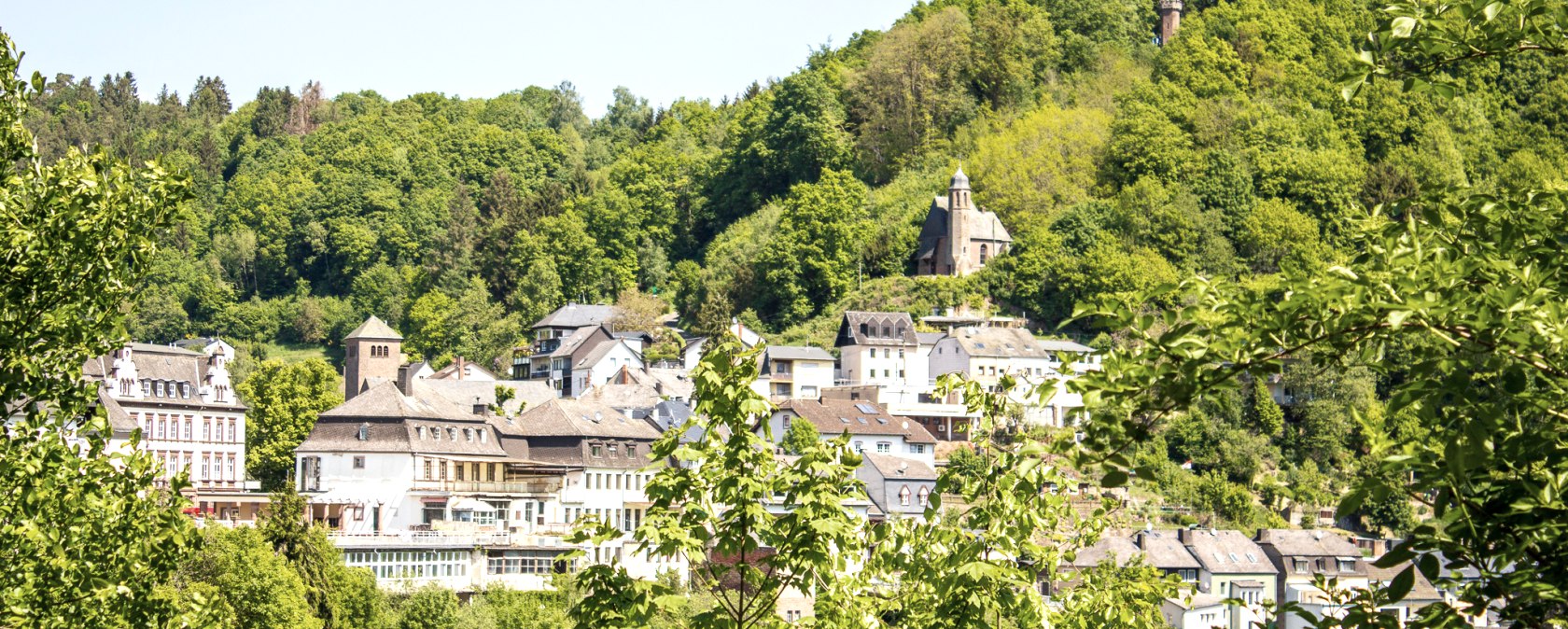 Gezicht op Kyllburg met historische gebouwen en een kerk, omringd door dichtbeboste heuvels onder een blauwe hemel., © Tourist-Information Bitburger Land_Monika Mayer