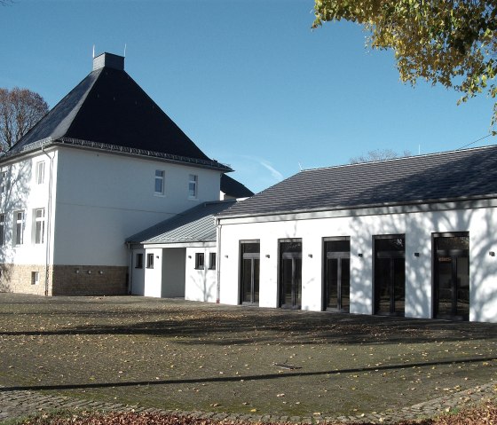Weißes Gemeindehaus Messerich mit dunklem Dach, umgeben von Herbstlaub und blauem Himmel. Startpunkt einer Wanderung., © O. Schröder