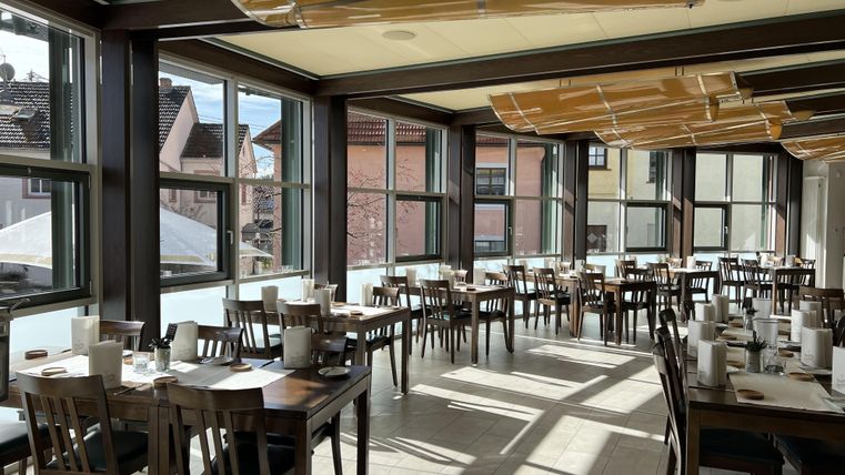 Ein modernes Restaurant mit vielen Holztischen und Stühlen. Große Fenster lassen viel Licht herein und bieten einen Blick auf die Außenseite.