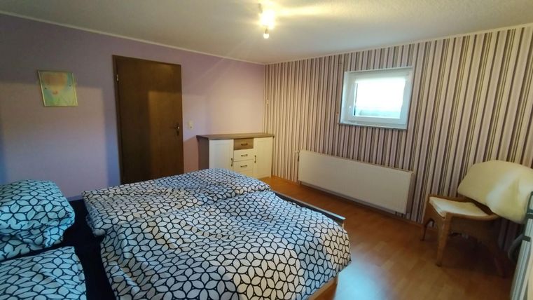 Ein gemütliches Zimmer mit einem großen Bett und einem modernen Kleiderschrank. Die Wände sind in sanften Farben gestrichen und mit Streifen dekoriert.