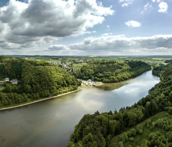 Luchtfoto van het Bitburg stuwmeer in Biersdorf am See, omgeven door groene bossen en heuvels onder een bewolkte hemel., &copy; Eifel Tourismus GmbH, Dominik Ketz