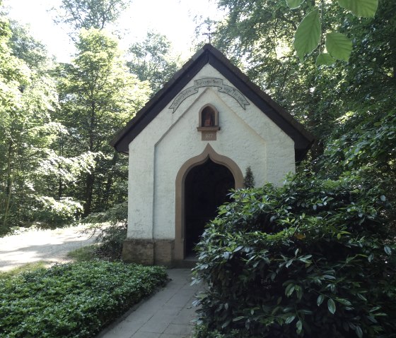 Petite chapelle dans la forêt de Speicherer, entourée d'une épaisse verdure. Un petit chemin mène à la porte d'entrée, entourée d'arbres et d'arbustes., © TI Bitburger Land