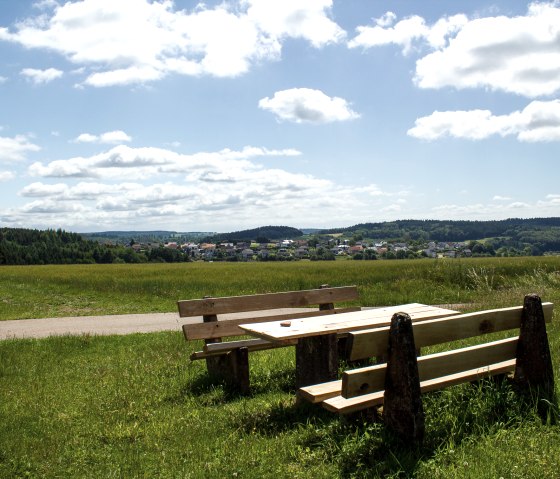 Holztisch und Bänke auf einer Wiese mit Blick auf Neidenbach und bewaldete Hügel im Hintergrund., © TI Bitburger Land - Monika Mayer