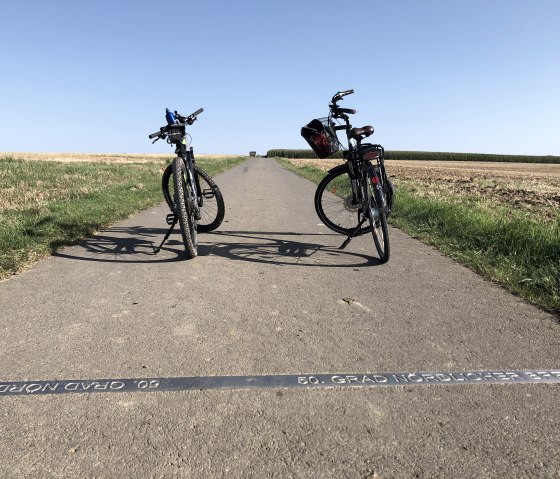 Twee fietsen staan geparkeerd op een landweggetje dat de 50e breedtegraad markeert. De lucht is helder en blauw., © Tourist Information Bitburger Land
