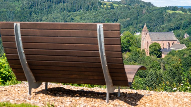 Holzbank mit Blick auf eine Kirche in einer grünen Landschaft.