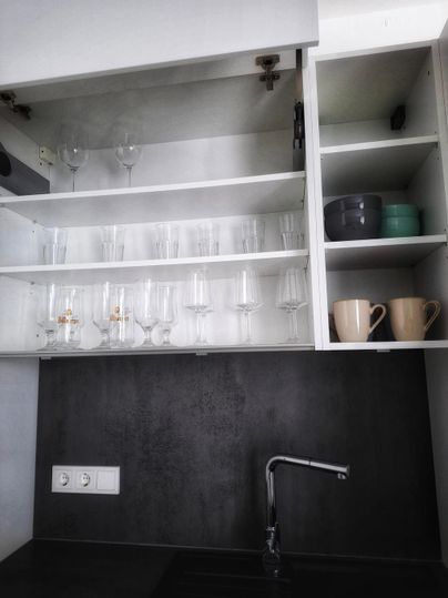 Un meuble de cuisine moderne avec de la vaisselle en verre et des tasses. L'espace de cuisine noir est bien organisé et rangé.