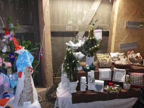 Ein weihnachtlicher Marktstand mit kleinen dekorativen Bäumchen und verschiedenen Geschenken. Die Atmosphäre ist gemütlich und festlich.