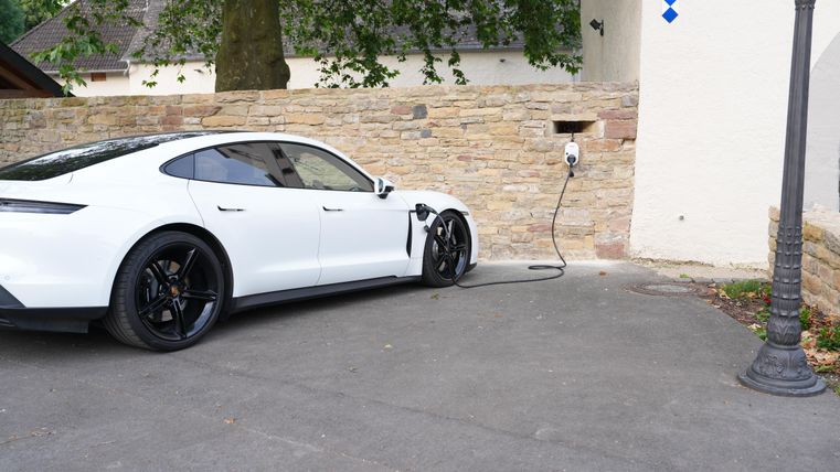 Een witte elektrische auto staat bij een laadpaal. Op de achtergrond is een stenen muur en een lantaarnpaal zichtbaar.