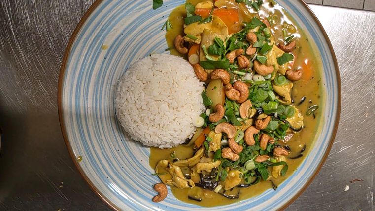 Ein buntes Gericht mit Gemüse und Cashewkernen, serviert mit Weißreis. Die Farben und Zutaten verleihen dem Essen ein ansprechendes Aussehen.