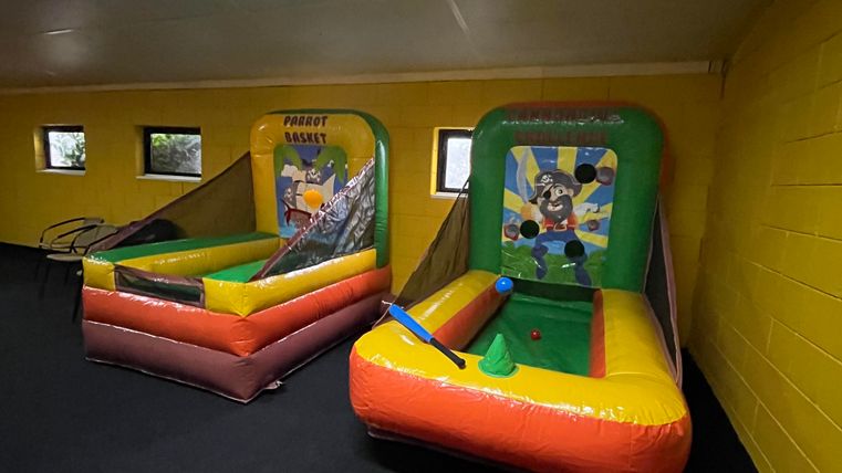 Ein farbenfrohes Hüpfburg-Spielbereich mit zwei aufblasbaren Spielen. Der Raum hat gelbe Wände und ist gut beleuchtet.