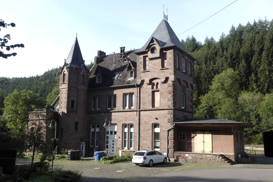 Historic red brick station building with towers, surrounded by trees and a parked car., © Eifelverein Ortsgruppe Speicher
