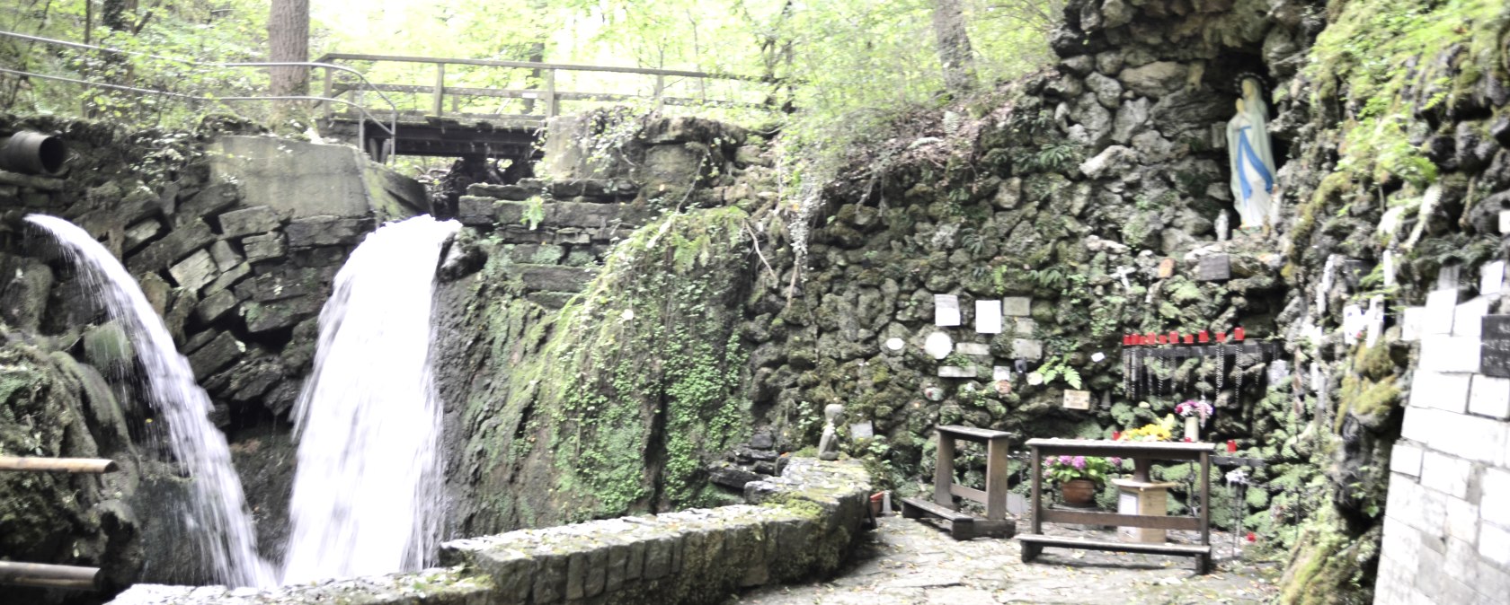 The Mariengrotte Albach features two waterfalls, a statue of the Virgin Mary in a rock niche and candles on an altar. Surrounded by lush greenery., © TI Bitburger Land