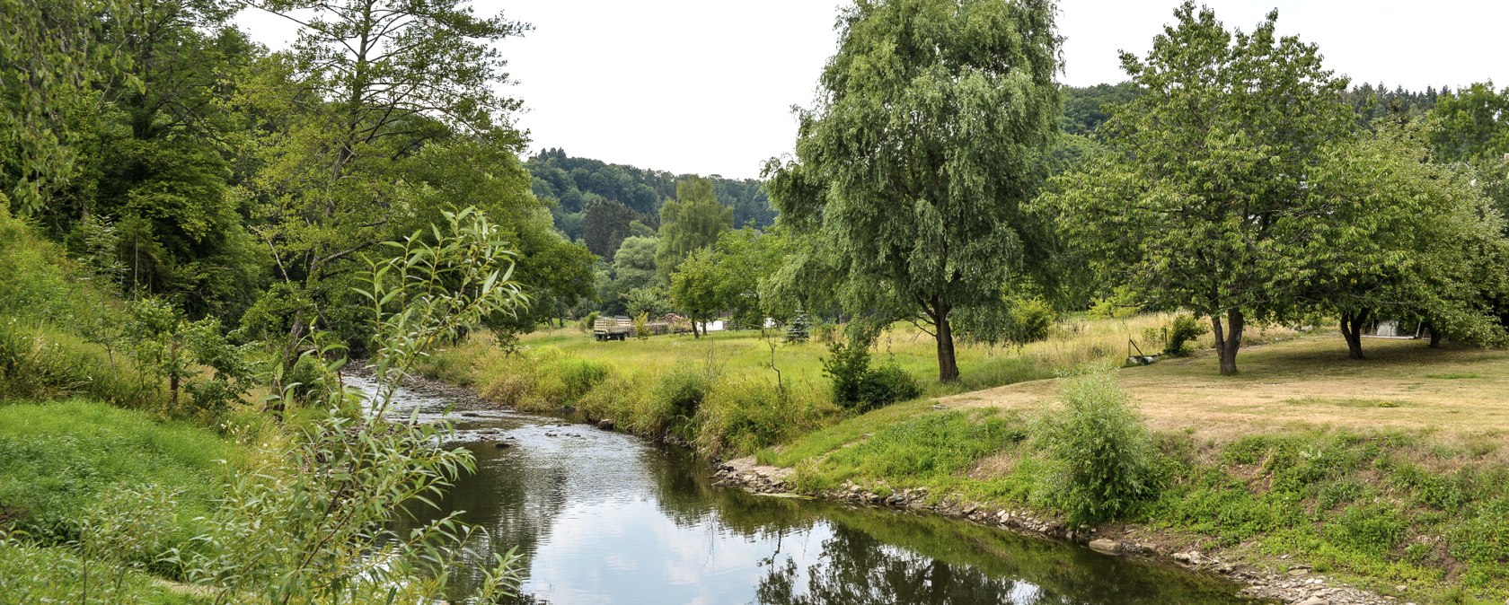 A small river meanders through a green landscape of trees and meadows. The sky is slightly cloudy., © TI Bitburger Land