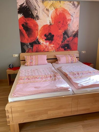 Ein gemütliches Schlafzimmer mit einem Doppelbett und pinken Bettläufern. Im Hintergrund ist ein großes, leuchtendes Gemälde mit roten Blumen zu sehen.
